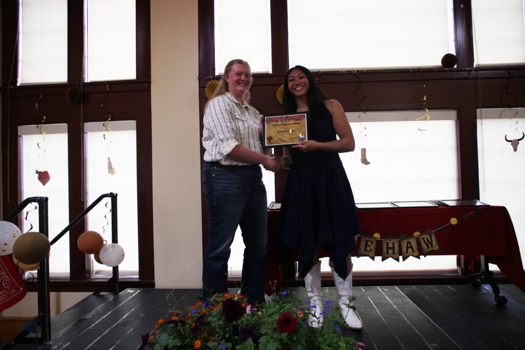 Two people stand together on a stage holding a framed award.