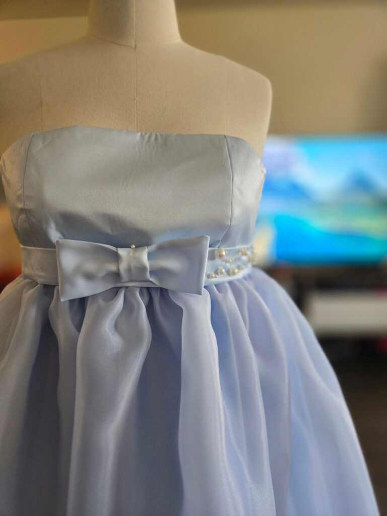 Close-up of a strapless, periwinkle-colored chiffon evening gown with a bow around the waist. The dress is pinned to a mannequin.