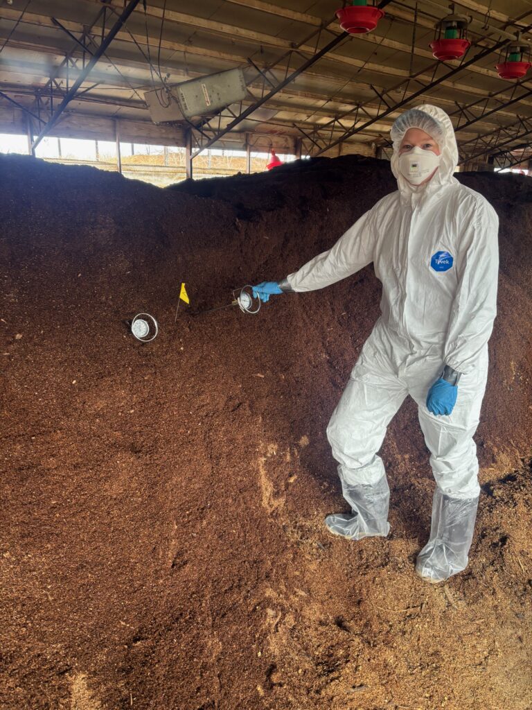 A person in personal protective equipment faces the camera while adjusting a temperature probe.