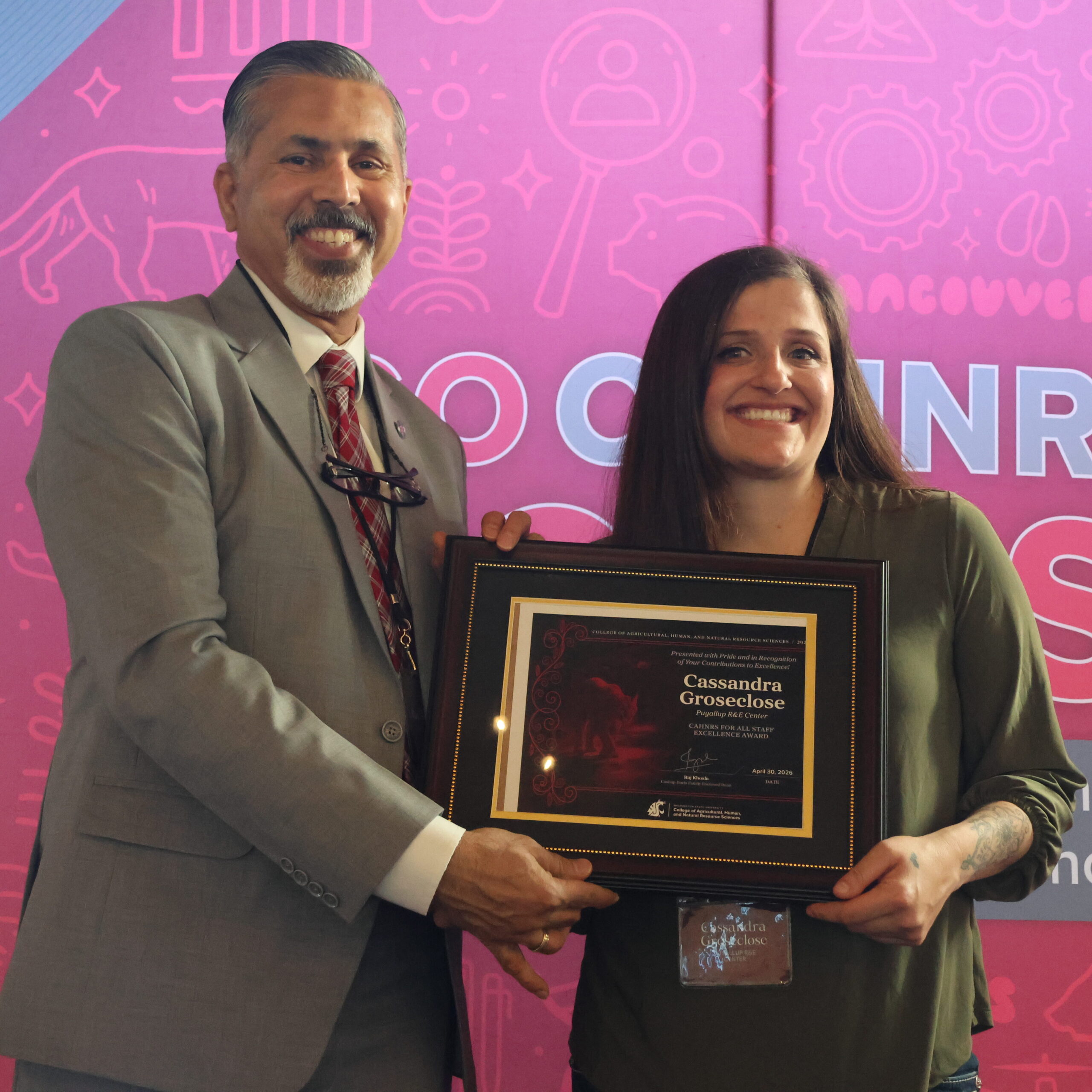 Groseclose, right, smiles in from of WSU themed crimson and gray backdrop, with Dean Khosla, both holding certificate.