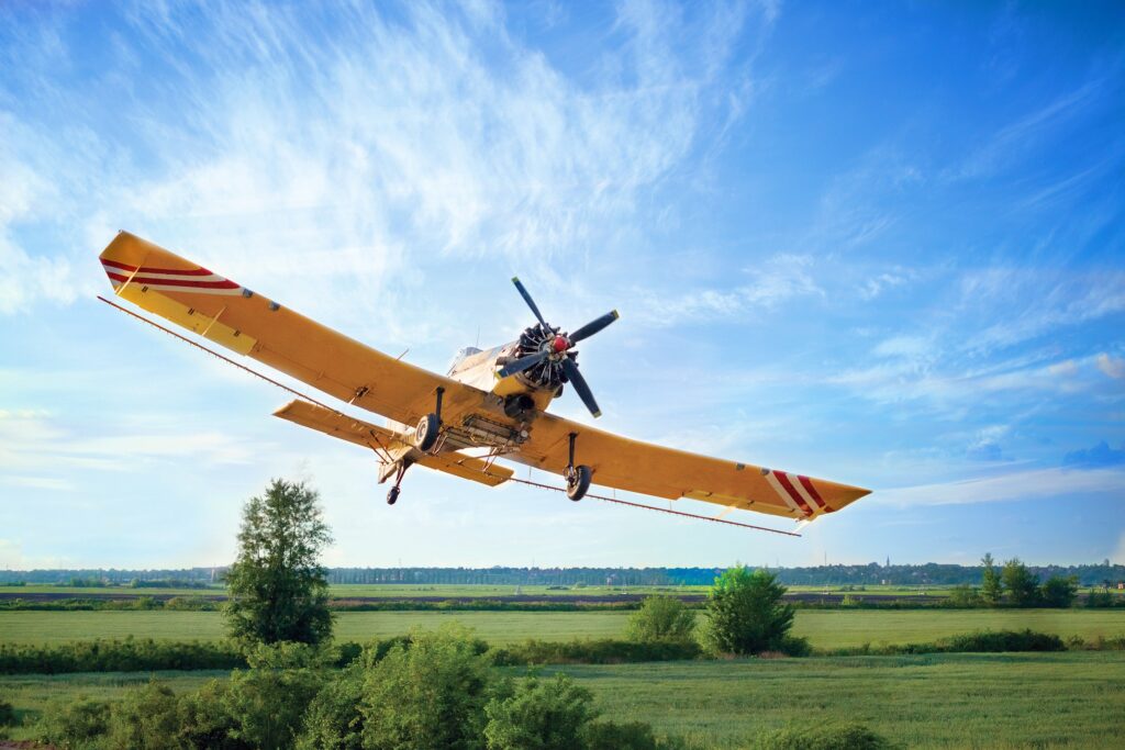 A agricultural plane dusts crops against a blue sky