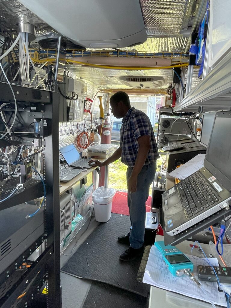 Adeniyi Olufemi Adesina, surrounded by technical, research grade equipment in a mobile laboratory, monitors the real-time measurements on a laptop.