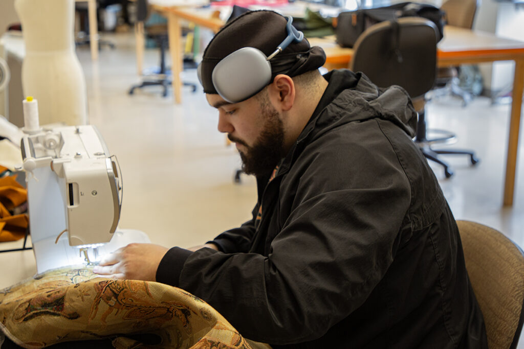 A person sits at a sewing machine with a piece of fabric being stitched together.