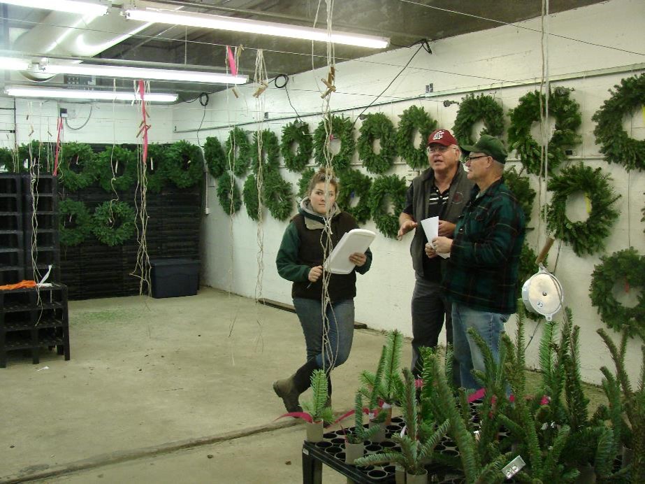 Three people consult together at the front of the room. They are surrounded by decorative greenery and wreaths.