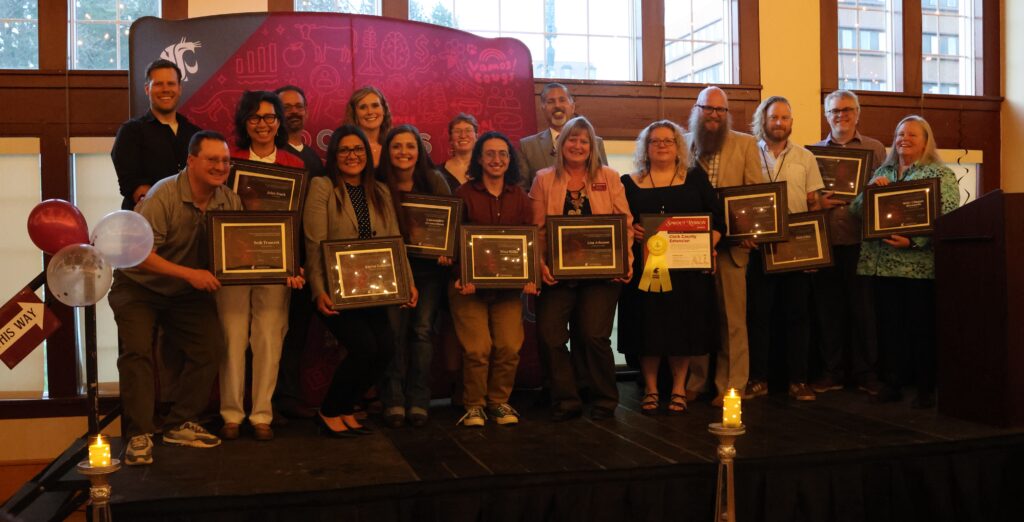 Posed group of award recipients with their certificates, on stage.