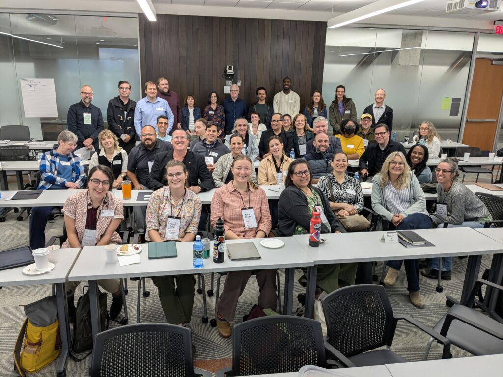 A group of people smile at the camera in a conference-style lecture room.