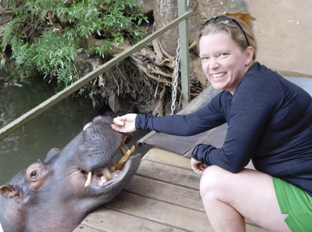 Kimberly Ange-van Heugten reaches down to touch a hippo in water.