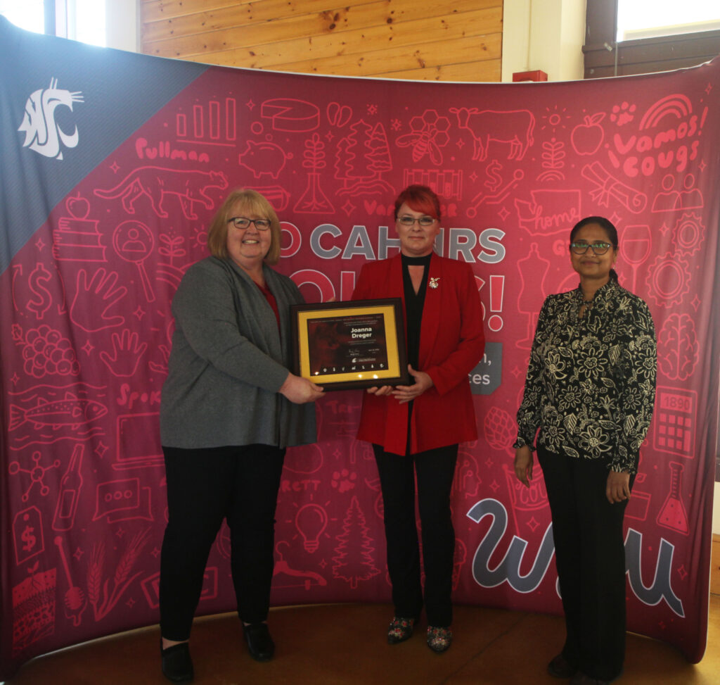 Three people stand together in front of a WSU CAHNRS-themed background. The two on the left hold an award.