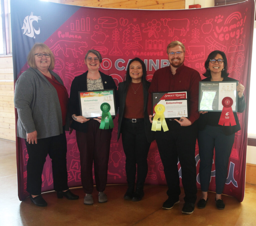 Five people stand in front of a WSU CAHNRS-themed background. Three of them hold awards with ribbons attached to them.