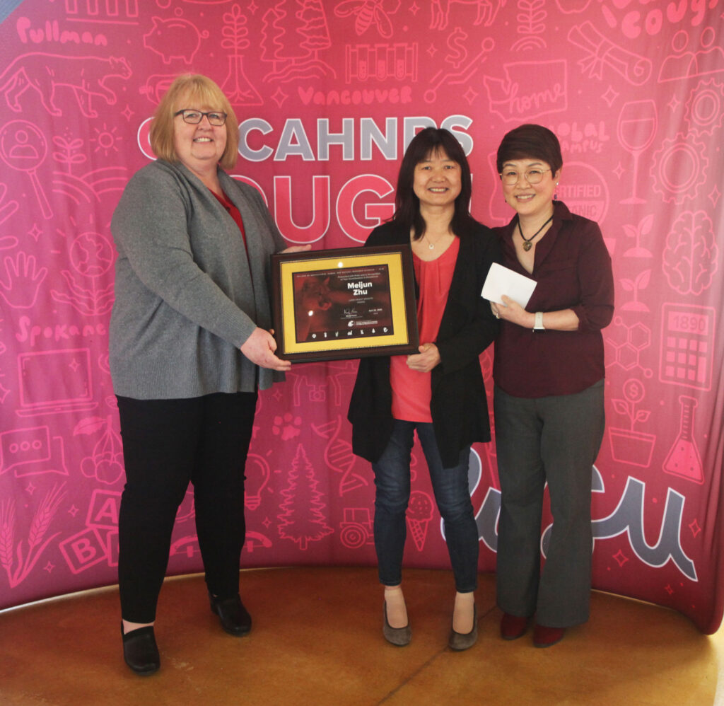 Three people stand together in front of a WSU CAHNRS-themed background. The two on the left hold an award.