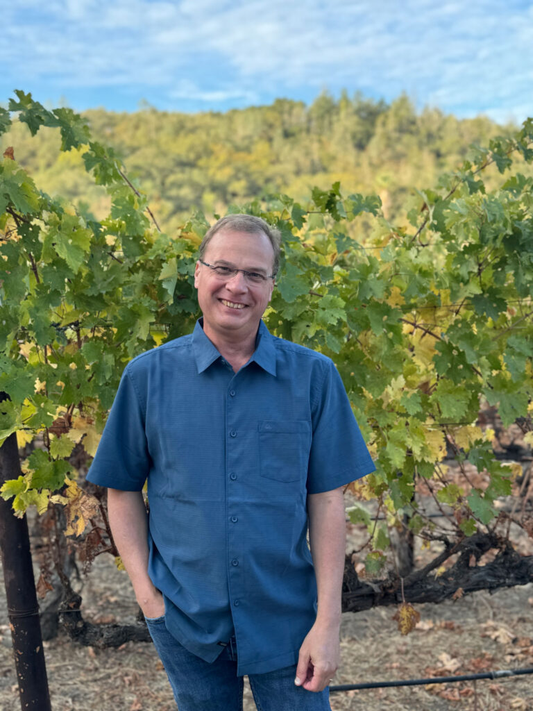 Bob Coleman stands in a vineyard in a button-down shirt.