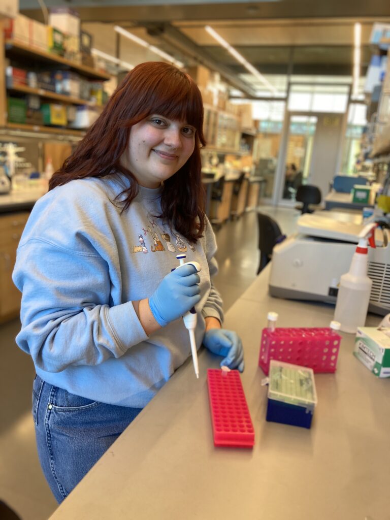Davenport, standing at a lab bench holding a pipette.