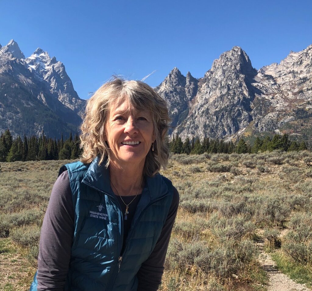 Melissa Hansen pictured in front of mountains, trees, and blue skies.