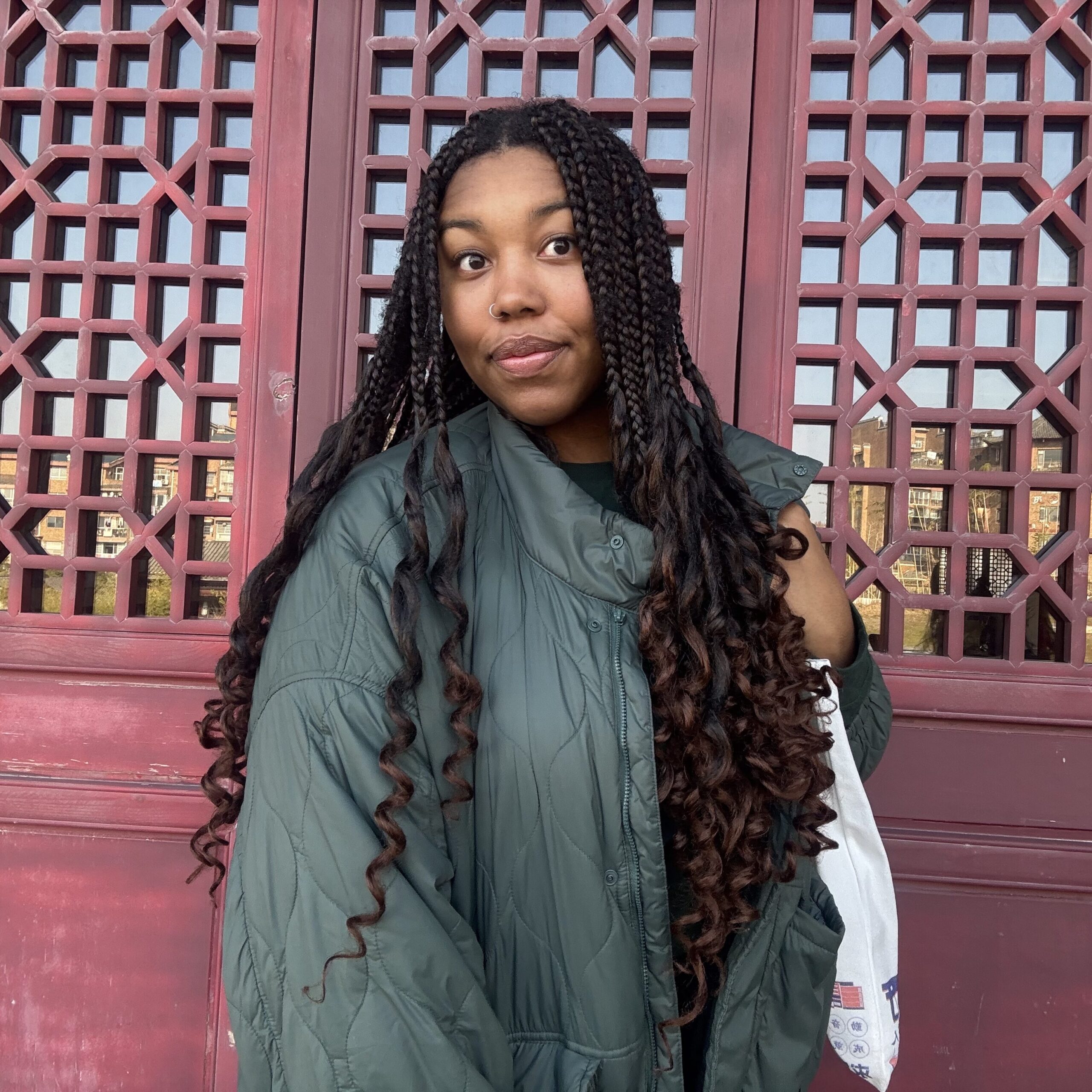 Alizee Hargrove standing in front of a red wood background with patterning in front of a mirror on the top half.