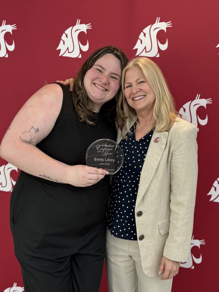 2 people pose against a crimson background, with one of them holding a glass award.
