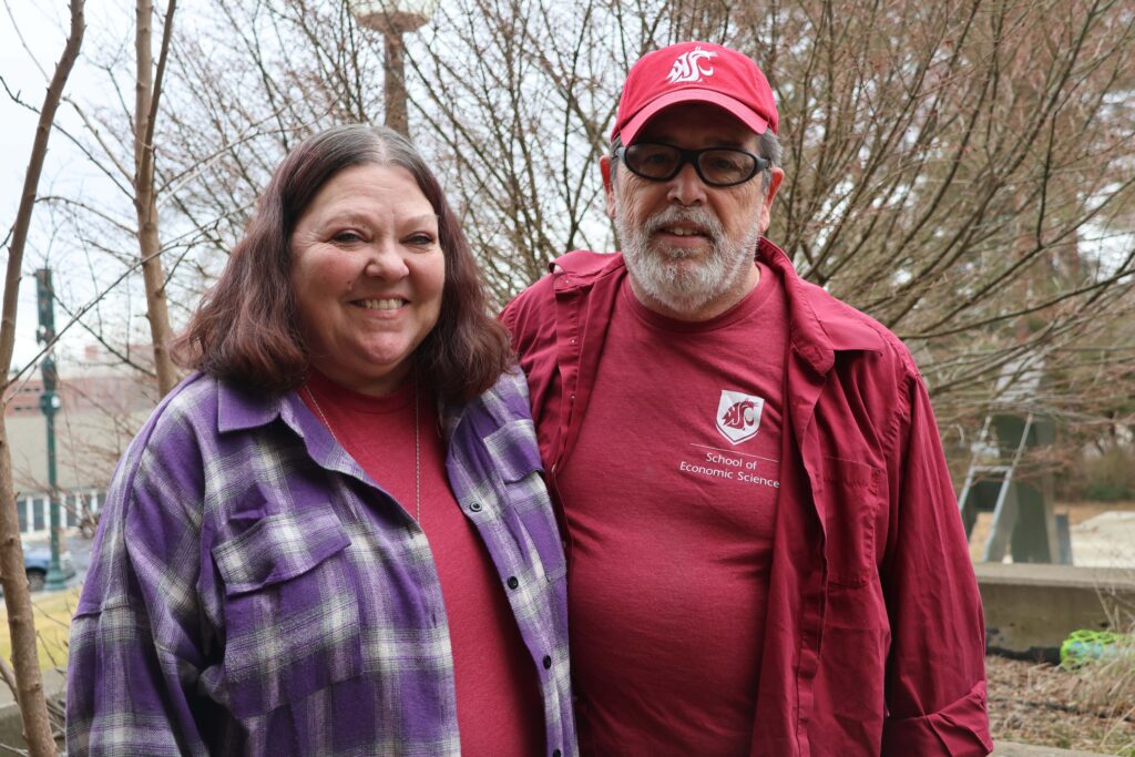 Jamie and Tom, smiling, face the camera in an outdoor campus setting.