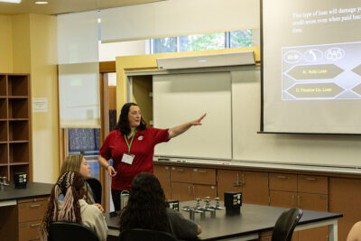 Kayla Wells-Yoakum gestures toward a projected slide at the front of a classroom while youth look on.