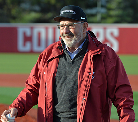 A person wearing a crimson WSU jacket walks on a baseball field.