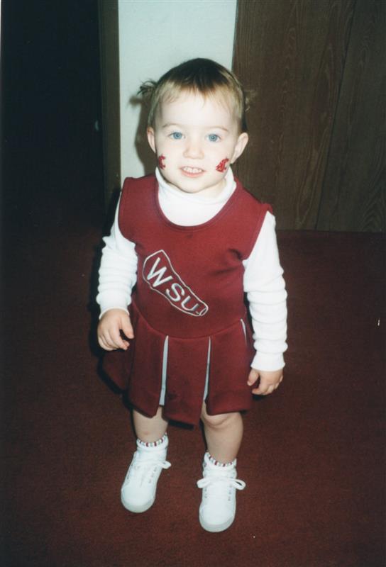 A toddler wears a WSU cheerleader uniform with WSU Cougar logos on each cheek.