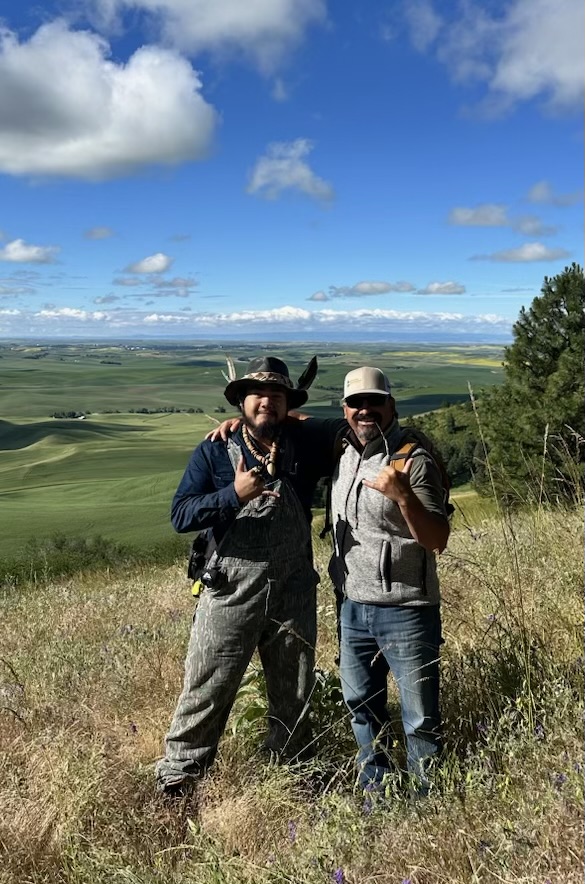 Two people pose on top of a bluff overlooking a dramatic view.
