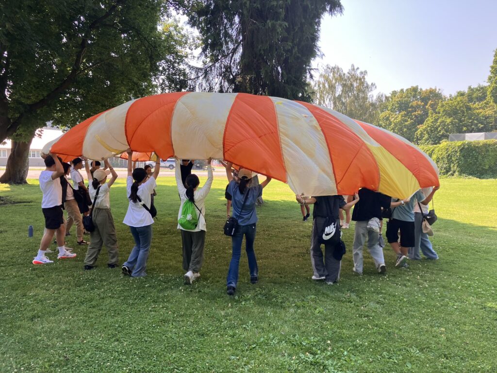 A dozen or so people stand around holding the edge of a circular parachute above their heads.