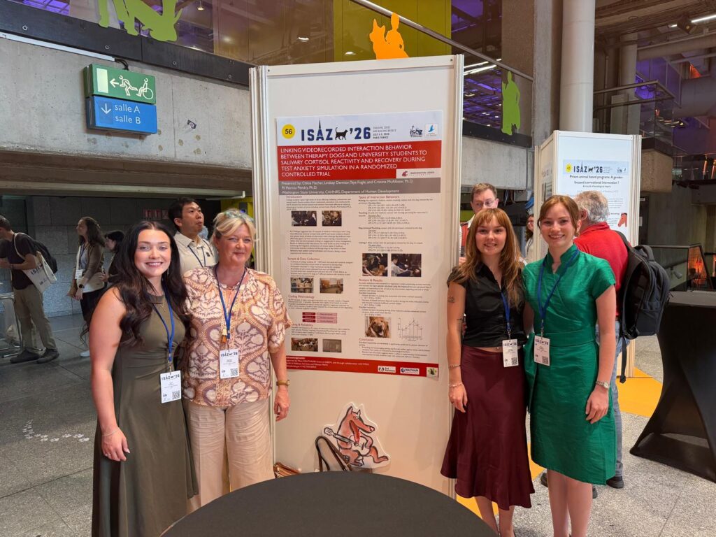 4 people stand around a large academic poster in a big open area.