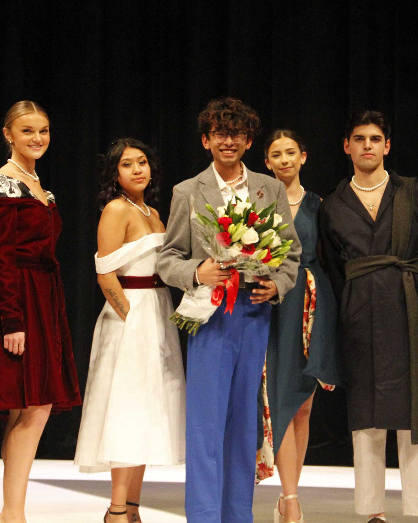 Stone Duran holding flowers on stage with four other students.