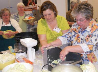 A group of people shredding cabbage and preparing foods in a kitchen.