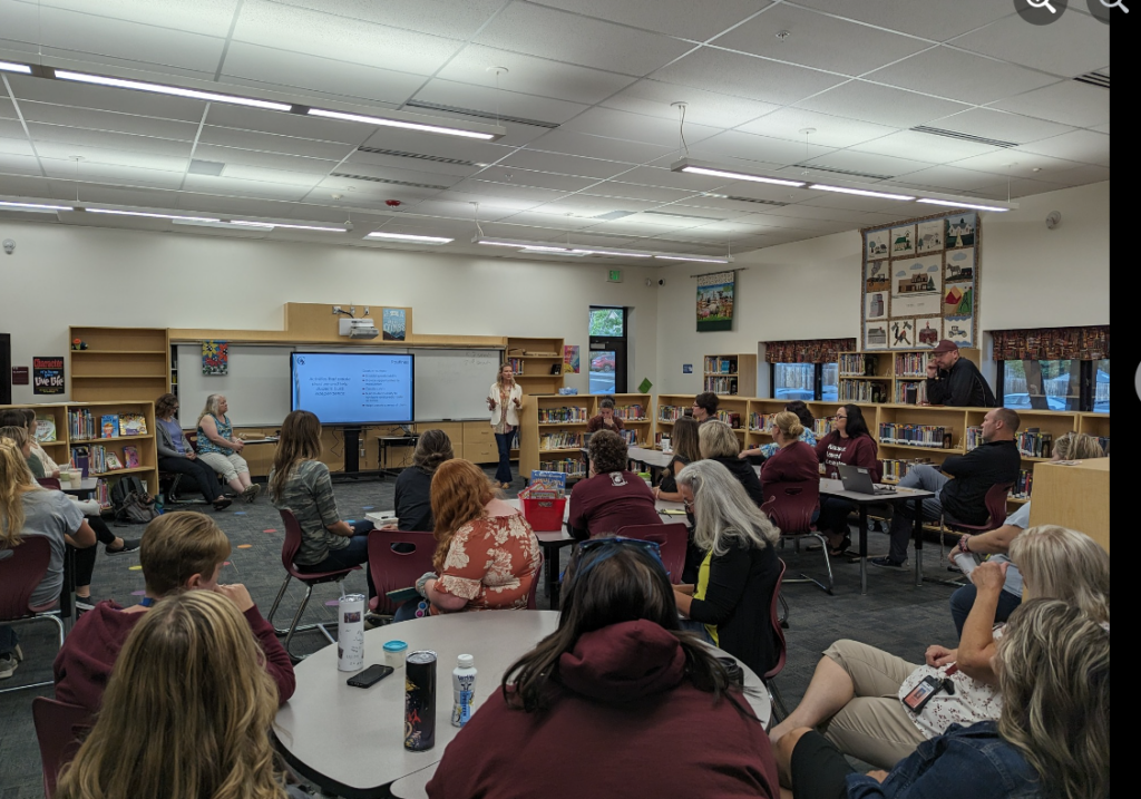 A group of people face the front of a room in an elementary school library during a presentation.