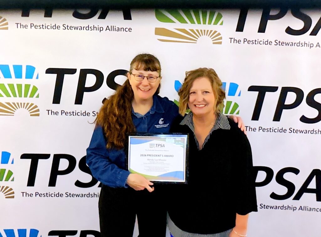 Wendy Sue Wheeler next to TPSA President Nicole Jansen. Wheeler holds an award certificate, and they stand in front of a repeating TPSA logo backdrop.