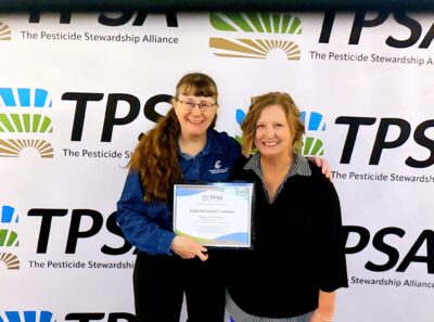 Wendy Sue Wheeler next to TPSA President Nicole Jansen. Wheeler holds an award certificate, and they stand in front of a repeating TPSA logo backdrop.