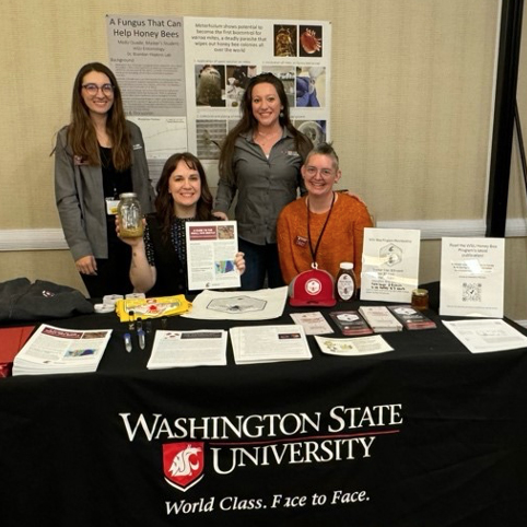 Four people with posters and brochures at a table with a Washington State University banner.