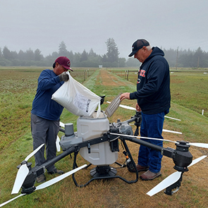 Two people in hats and jackets pouring contents of a bag into a drone.