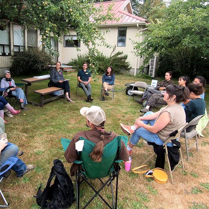 People in a circle of lawn chairs in an outdoor educational setting.