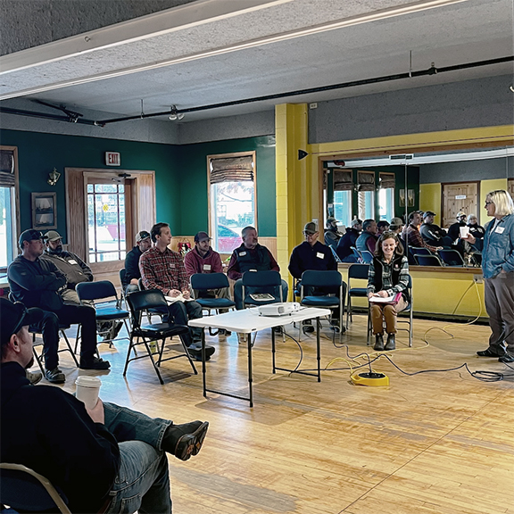 Person with a microphone addressing small group seated in folding chairs.