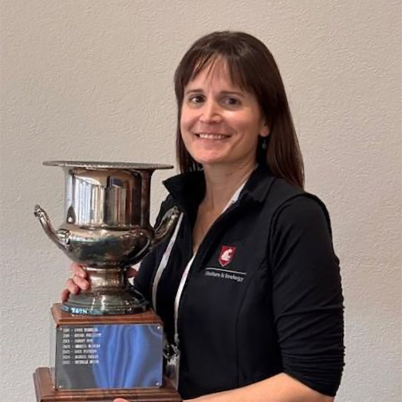 Smiling person with WSU jacket holding a trophy.