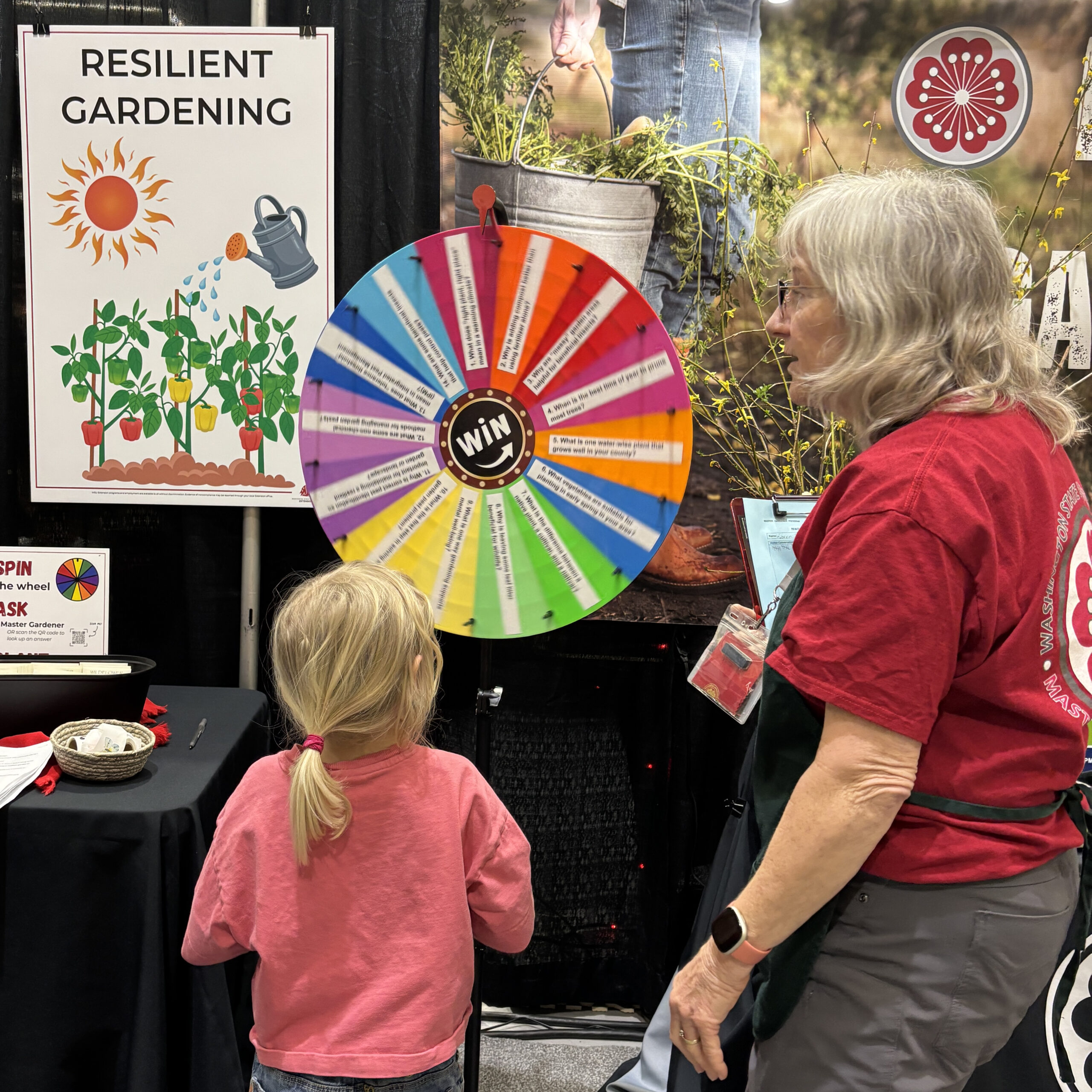 A child and an adult spin a colorful wheel adjacent to a sign reading “Resilient Gardening.”