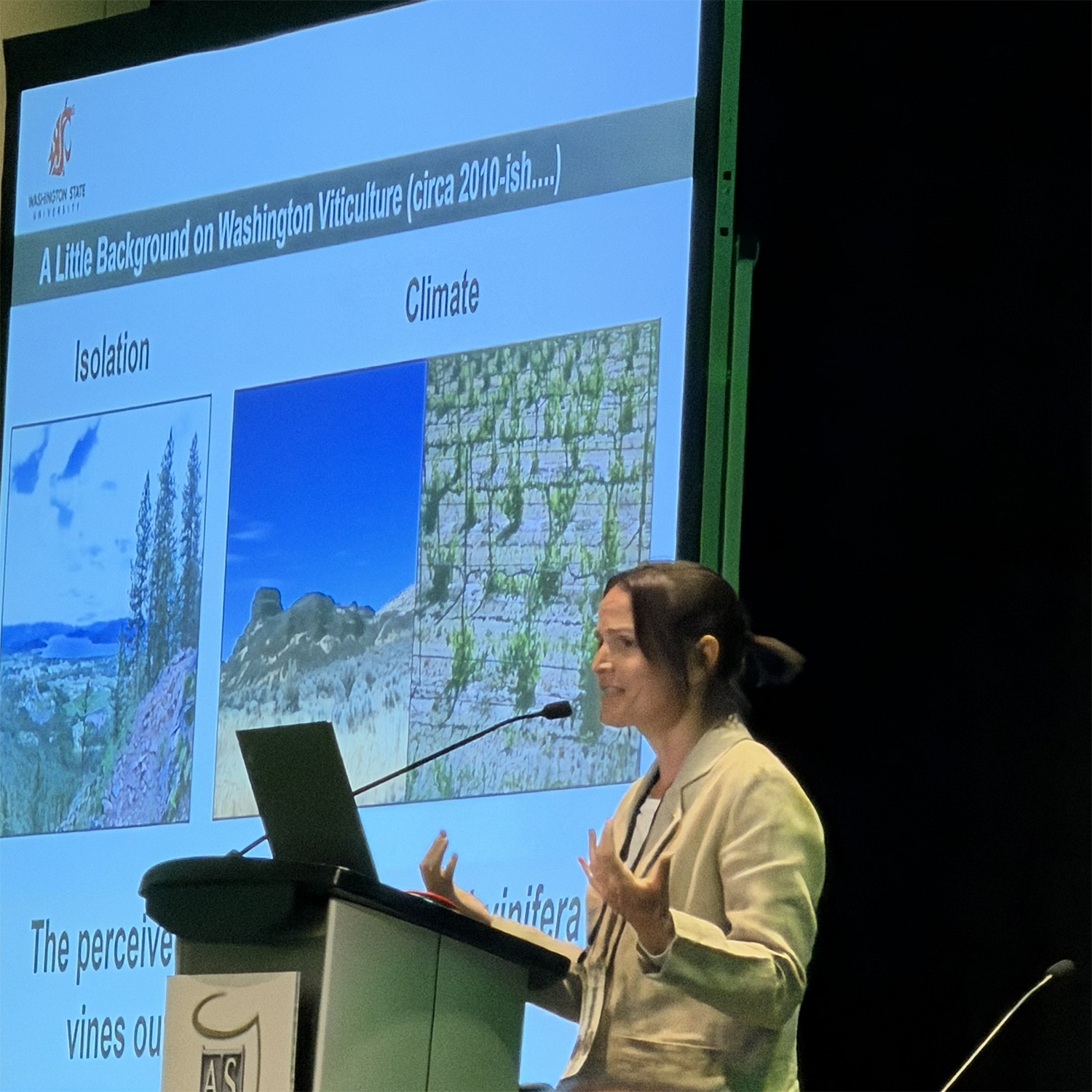 A person at a podium with vineyard photos in the background.
