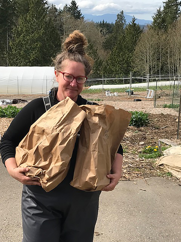 Woman in overalls holds two brown paper bags full of sweet potato starts.
