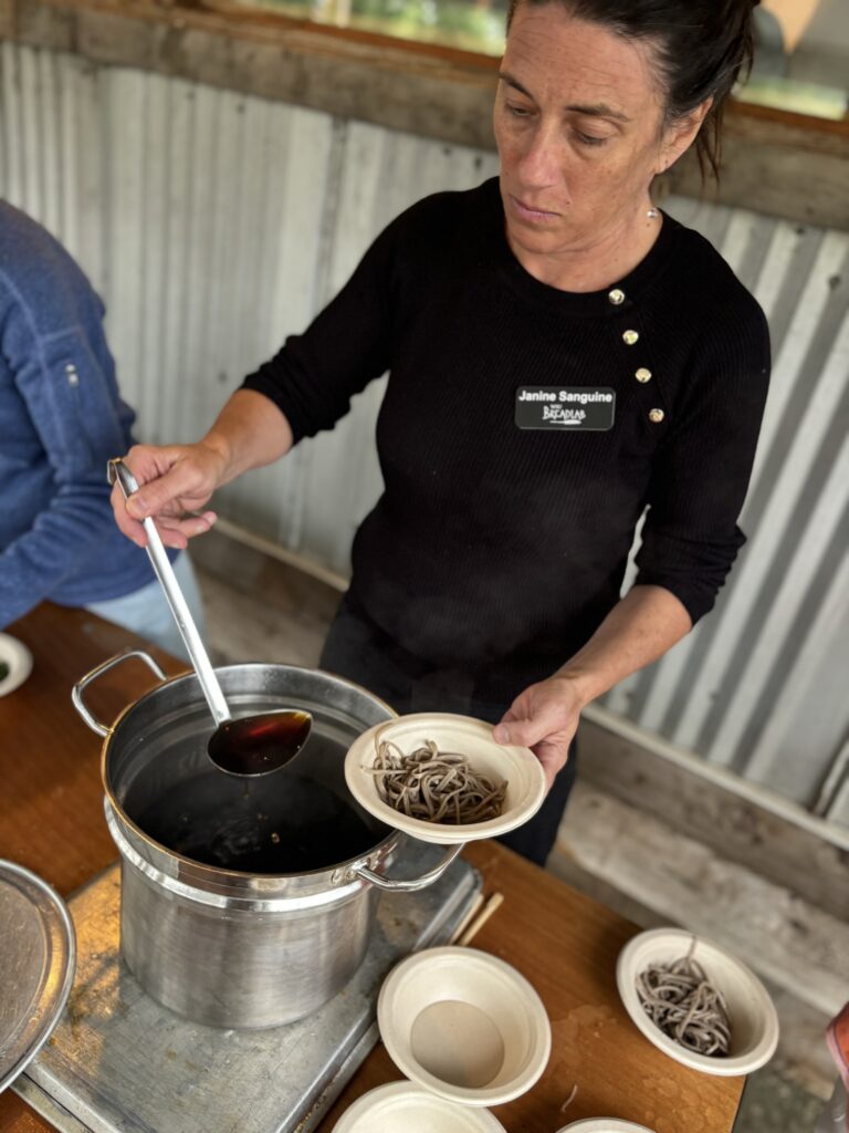 Woman scooping broth out of a pot into a bowl filled with noodles