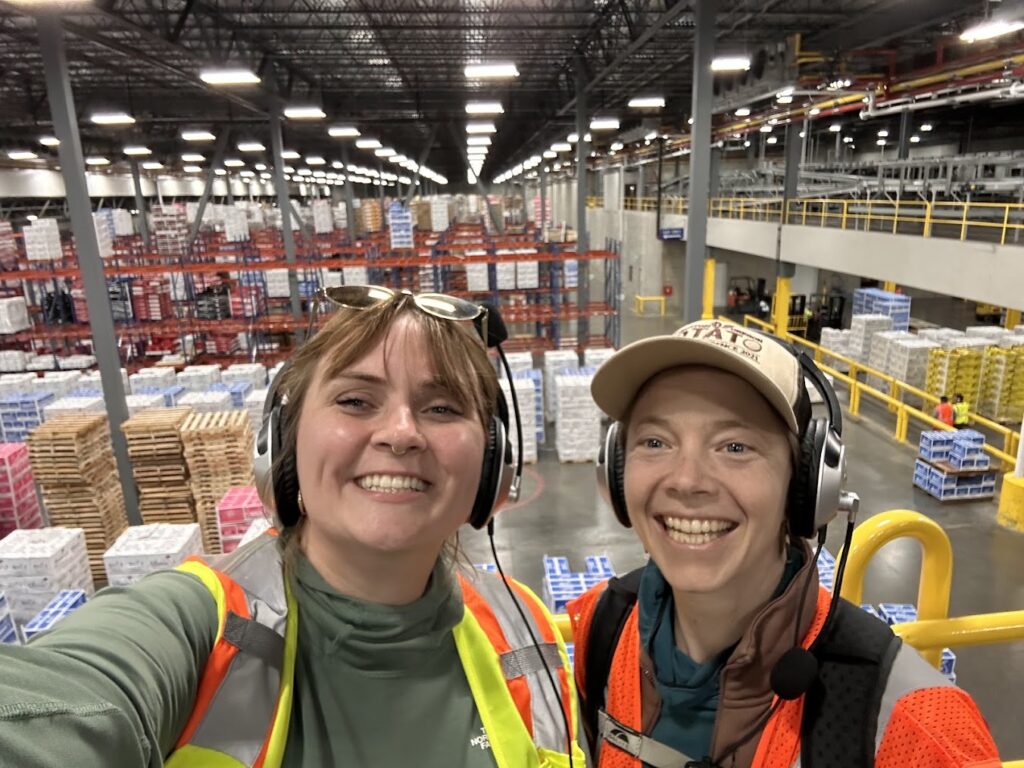 Two women pose for a selfie while touring a fruit packing plant.