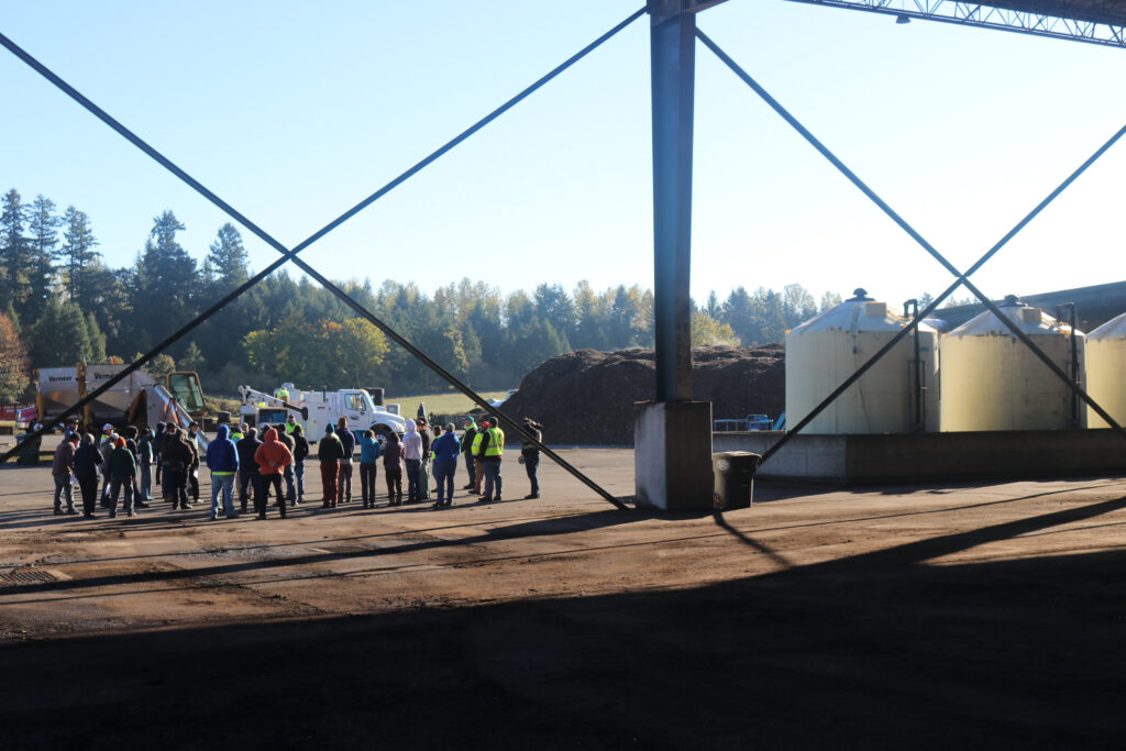 People standing outside in bright sun near compost heaps.