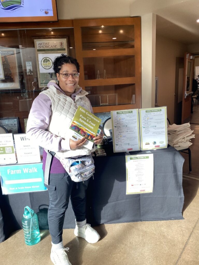 A young woman holds information in front of a table setup at a conference.