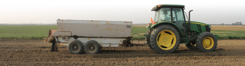 Tractor pulling trailer that's spreading biochar on field.