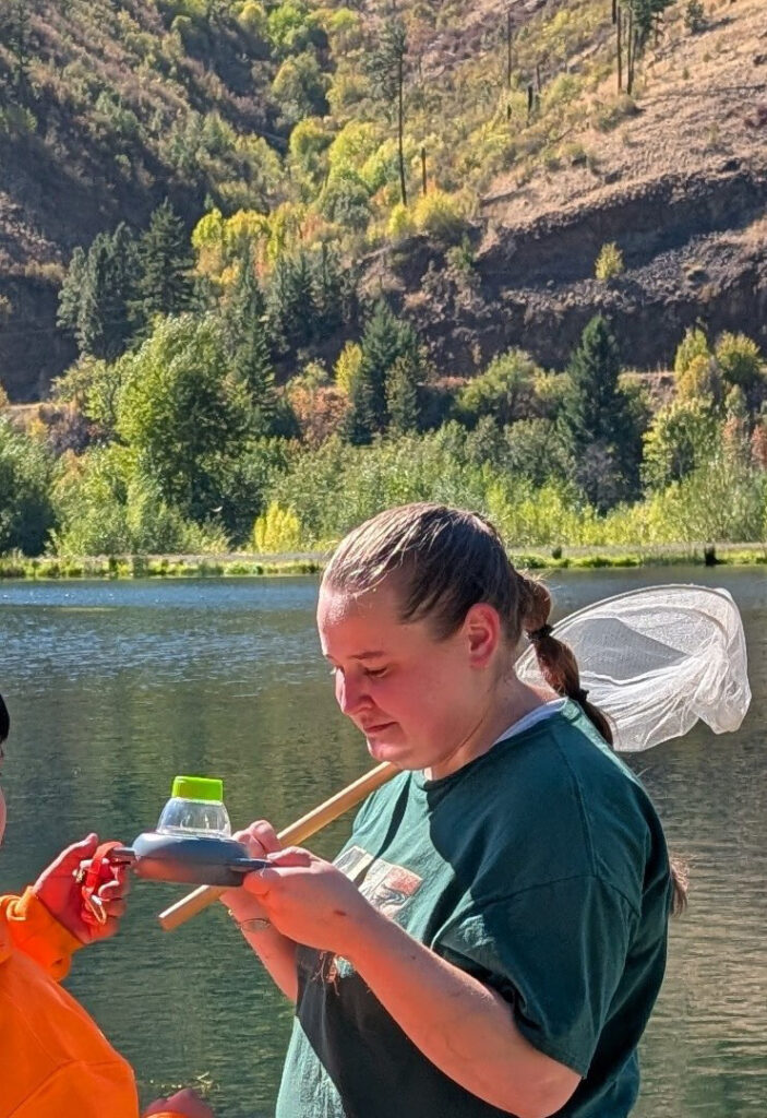 A woman holds an insect net while st standing outdoors near a body of water.