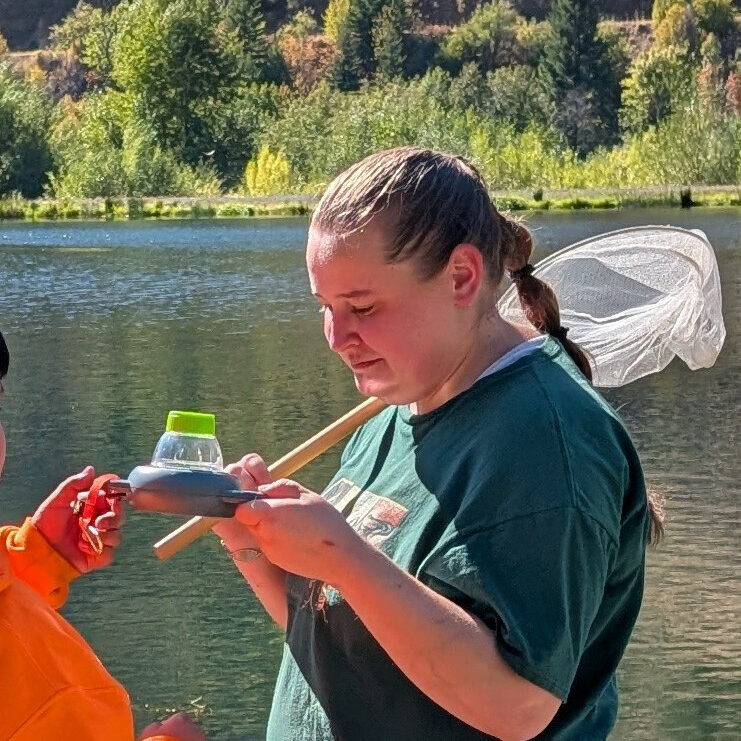 A woman holds an insect net while st standing outdoors near a body of water.