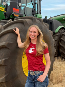 A young woman stands in front of a tractor.