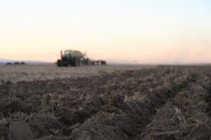 Soil furrows in a field with a tractor in the background.