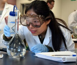 Woman in goggles with laboratory flask and notebook