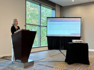 Person standing at podium, next to a projected slide. 